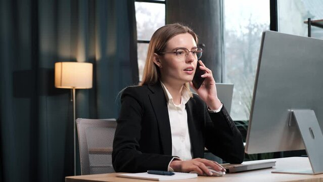 Smiling young business woman professional talking on phone using laptop sit at home office desk, happy female customer make mobile call confirming online website shopping order delivery concept