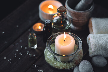 Spa setting with essential oil, candle, sea salt, pebbles, towel on dark wooden background. Massage, aromatherapy. Natural organic ingredients for relaxation, detention. Wellness in salon concept