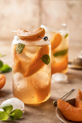 Fresh cold apricot cocktail, fizz or ice tea with mint leaves and garnish. Pink beige tile...
