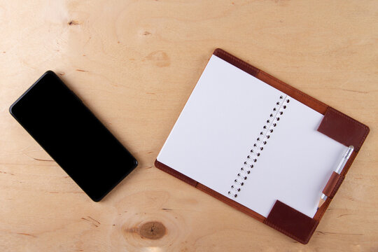 Digitalization concept. Paper notebook vs smartphone. Digital phone with blank black screen and empty  pocketbook lie on wooden table