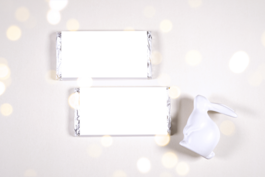 Party favor chocolate treat wrapper product mockup. Happy Easter theme product mockup. Minimal styling with bunny rabbit against a bokeh party lights background. Negative copy space.