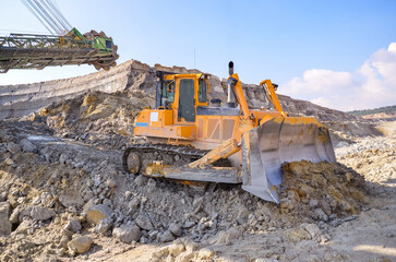 Obraz premium Crawler bulldozer working on construction site or quarry. Mining machinery moving clay, smoothing gravel surface for new road. Earthmoving, excavations, digging on soils
