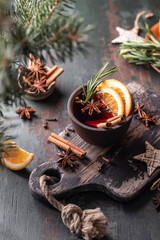 Mulled red wine in ceramic bowl with spices, fruits and rosemary on wooden rustic table, dark key. Traditional hot drink at Christmas time and winter