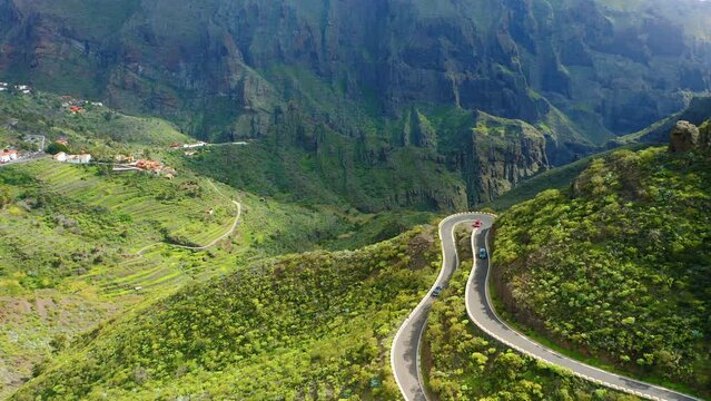 Cars driving through sharp turn on winding zig zag serpentine road in mountains. Narrow highway in beautiful lush green spring landscape. Tenerife Canary Islands Spain Europe.