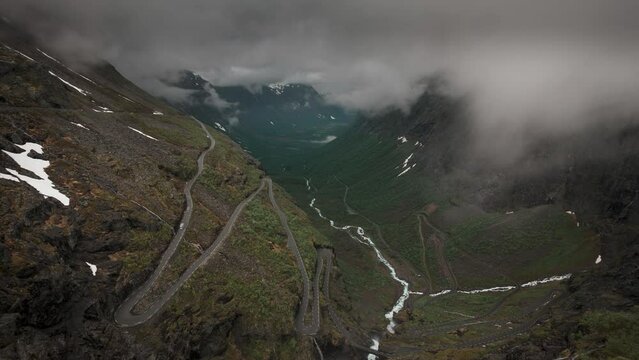 Timelapse video of mountain road Trollstigen winding through landscape with waterfall and valley of Trollveggen in Norway, dramatic sky with dark moving clouds, from above