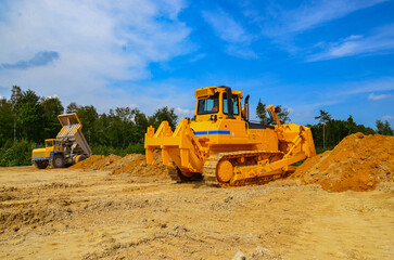 Big crawler dozer working on construction site or quarry. Mining machinery moving clay, smoothing gravel surface for new road. Earthmoving, excavations, digging on soils