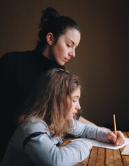 A young ukranian mother helps her daughter write a letter or do her homework. The concept of school lessons, learning and distance education.
