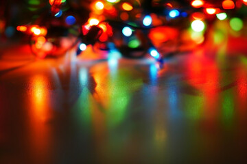 New Year's light-emitting diode garland burning in the dark close-up on a glossy surface, reflection multi-colored lights blur background