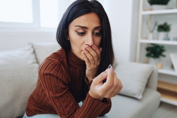 A woman looks sadly at a wedding ring in her hand, divorce and loss of a partner, breakup, unhappy heartbreak sitting at home on the couch