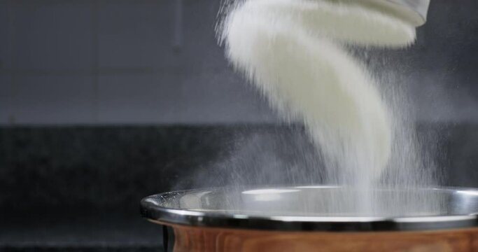 Experienced bakery chef sifting flour through sieve into the bowl, making bread, professional kitchen, closeup slow motion