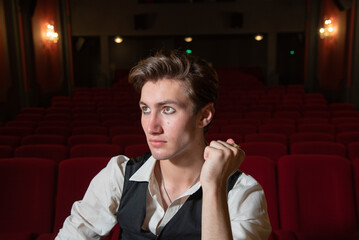 portrait d'un jeune homme dans une salle de cinema ou de spectacle avec des fauteuils rouges