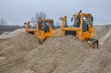 Obraz premium Crawler bulldozers working on construction site or quarry. Mining machinery moving clay, smoothing gravel surface for new road. Earthmoving, excavations, digging on soils