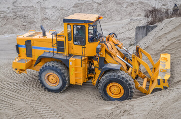 Wheel loader working in a gravel pit. Mining machines moving clay, smoothing the surface of gravel for a new road. Earthworks, excavations, digging in the ground, loading of charging baskets