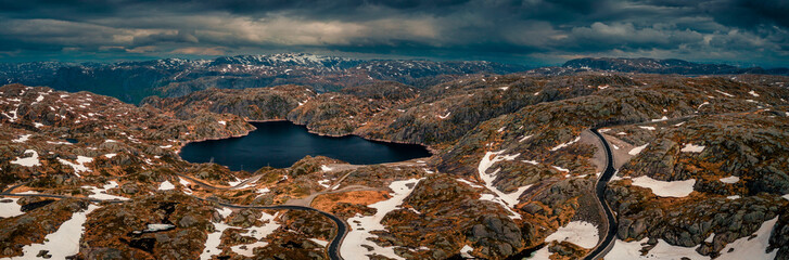 Landscape with lonesome road from above around Lysefjord in Rogaland with lakes and snow in Norway, dark cloudy sky - 559022188