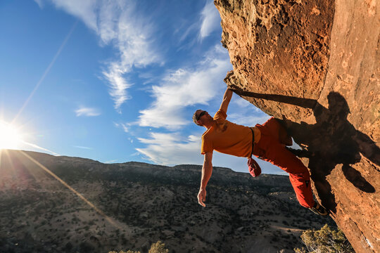 A rock climber hangs from one hand off a boulder near Grand Junction, Colorado.