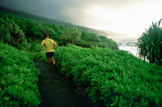 A trailrunner runs along a ocean trail on Maui.