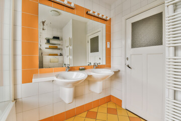 a bathroom with orange and white tiles on the walls, two sinks and a mirror in the wall behind it