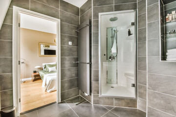 a modern bathroom with grey tile walls and white trim on the shower door, toiletries and mirror in...