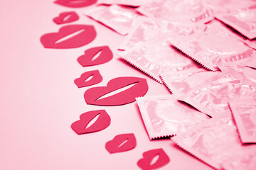 Many white packages of unopened condoms with paper kisses on a pink background.