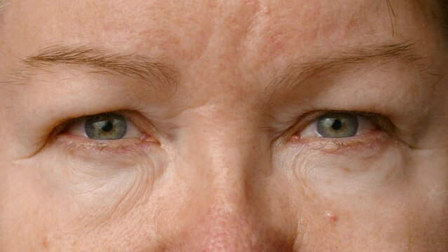Close-up view of an elderly woman. the woman opens her eyes and looks into the camera. The skin of an elderly person. Senior woman eyes, wrinkled face