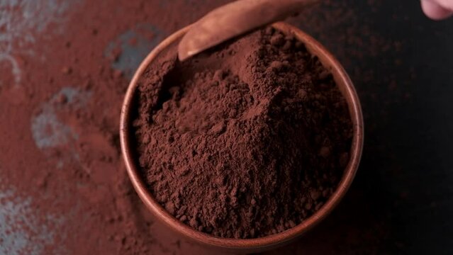 Spoon scooping cocoa powder from bowl on dark background.