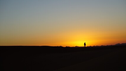 Fototapeta na wymiar A lone man walking on the edge of a sand dune belonging to a moroccan Sahara erg at sunset, near the settlement of Merzouga.