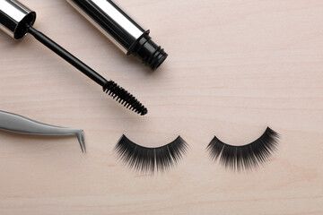 Naklejka premium Flat lay composition with false eyelashes, mascara brush and tweezers on wooden table