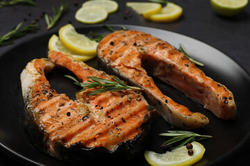 Plate with tasty salmon steaks on black table, closeup