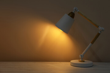 Fototapeta na wymiar Stylish modern desk lamp on wooden table at night, space for text