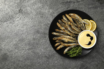Plate with delicious fried anchovies, lemon, microgreens and sauce on grey table, top view. Space...