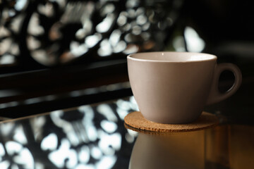Cup with cork coaster on black table in cafe, closeup. Space for text