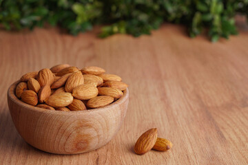 Tasty almonds in bowl on wooden table, space for text