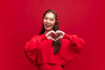 Young asian woman wearing red sweater dress shapes heart gesture on red background for Chinese new...