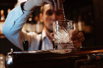 bartender prepares a cocktail with ice in a glass at the bar in a restaurant