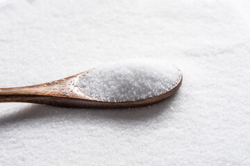 white salt crystals in a spoon on salt background.