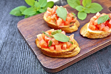 Bruschetta with tomato and basil on dark wooden board
