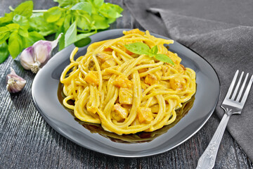 Spaghetti with pumpkin and bacon in plate on dark board