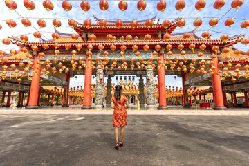 Rear view of Asian woman in red cheongsam qipao dress is visiting the Chinese Buddhist temple...