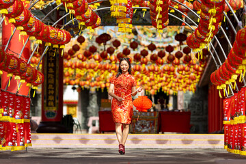 Obraz na płótnie Canvas Asian woman in red cheongsam qipao dress holding lantern while visiting the Chinese Buddhist temple during lunar new year for traditional culture concept