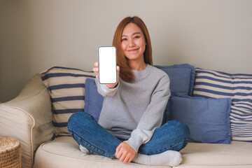 Mockup image of a young woman holding and showing a mobile phone with blank white screen while...