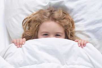 Kid under covers, face cover with blanket. Child wakes up in the morning in the bedroom. Cute...