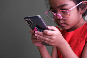 Little girl in red, sitting and busy playing with her gadget