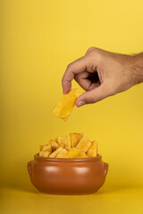 A hand picking up a fried manioc on top of portion of fried maniocs ( Mandiocas ) on a on a yellow...