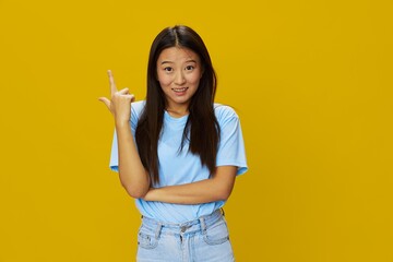 Asian woman smile with teeth hand gestures, signs and symbols on yellow background in blue t-shirt and jeans