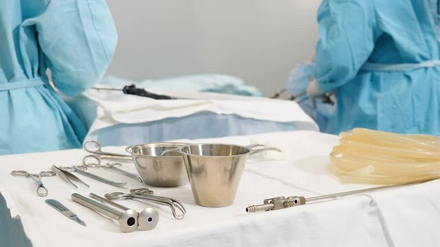 Laparoscopic scissors and graspers on white desk ready to be used at operation. Multifunction Laparoscopic Instruments. Close up of female and male doctor hands in sterile gloves while laparoscopy