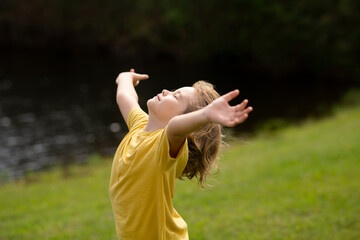 Peaceful kid with raised hands meditating, feeling calm positive and relaxed on nature background....