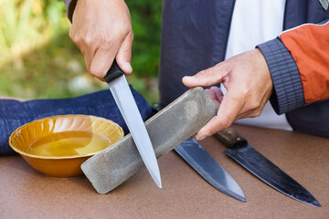 Closeup man hands sharpen knife on whetstone sharpener or grindstone. Concept, maintenance tools...