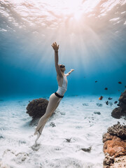 Freediver lady glides underwater near corals with tropical fish and sunset or sunrise sunlight in...