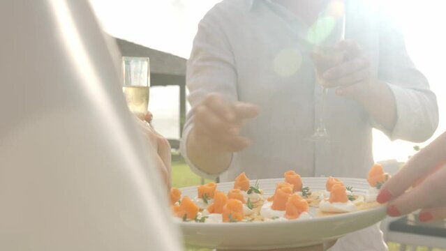 Woman serving canapes outdoors on the event, people holding champagne glasses and taking snacks