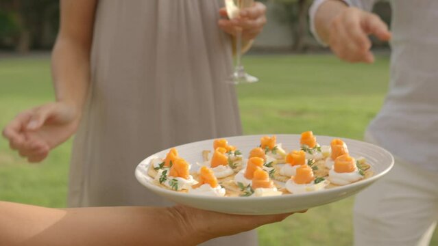 A plate with canapes outdoors, served for group, people take snacks from the plate